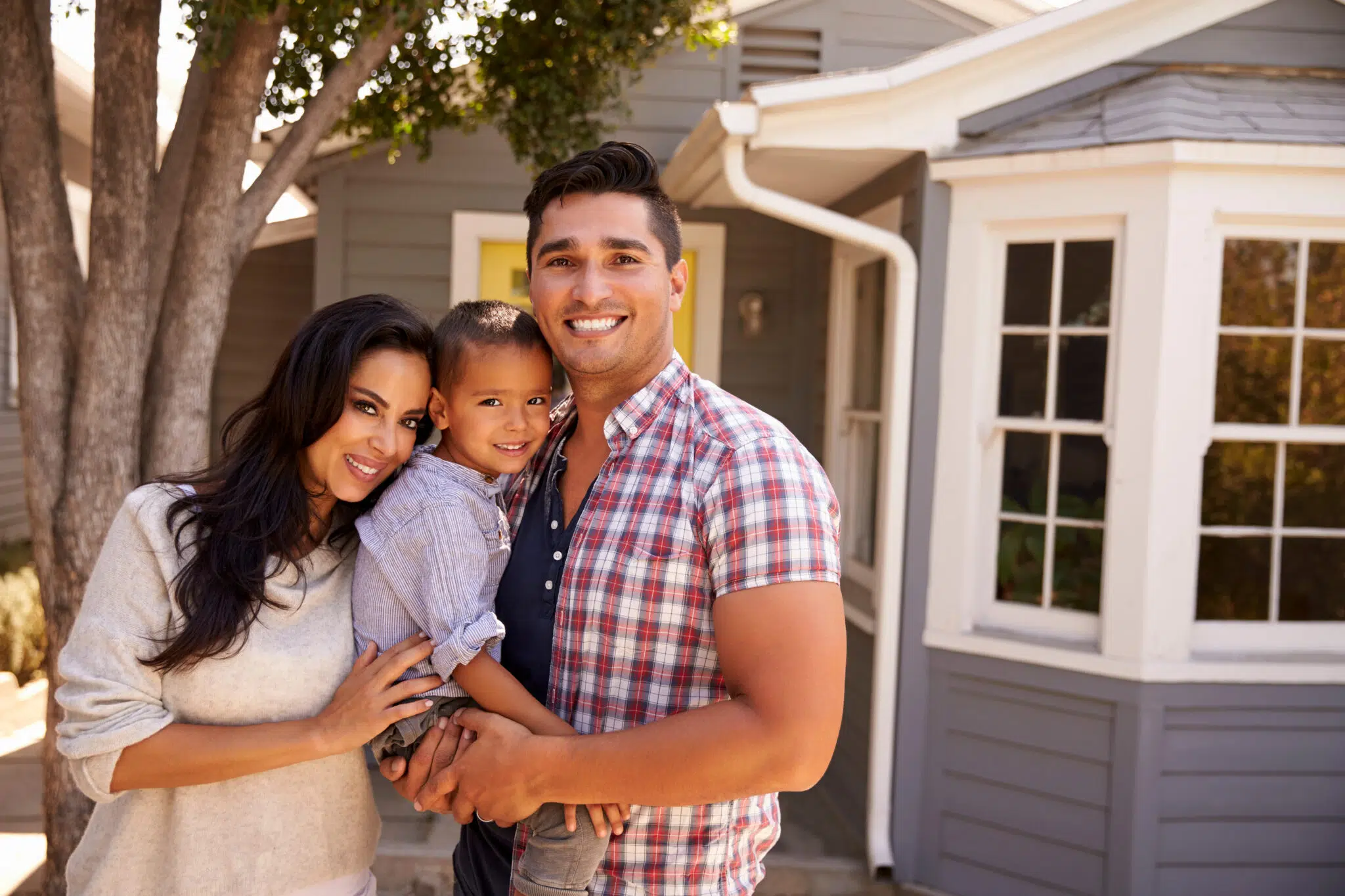 A happy family of three stands in front of their home | Family Lawyers | The Berdugo Law Firm