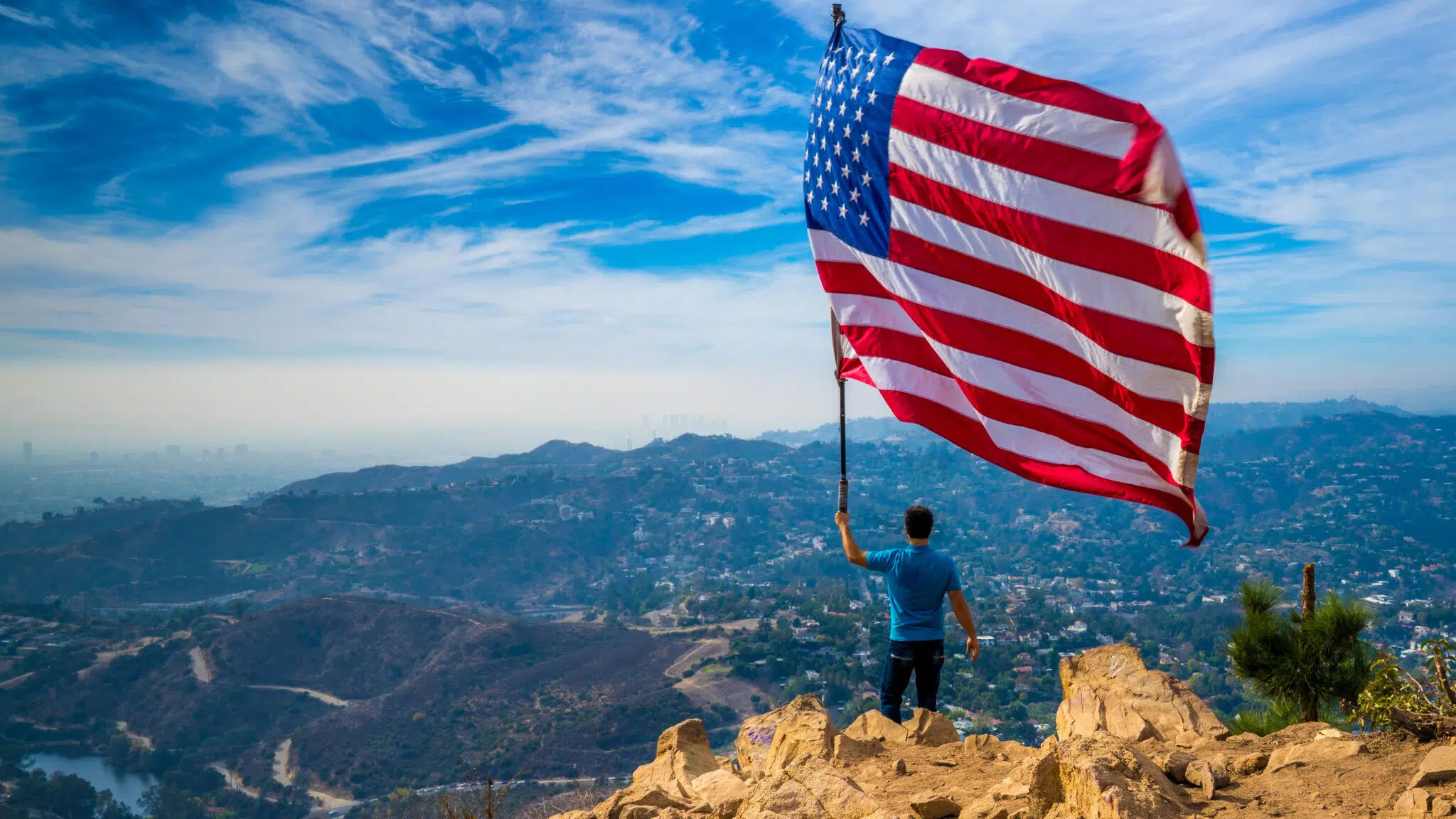 A patriot raises a U.S. flag at the mountain peak | Trusted Family Lawyers | The Berdugo Law Firm