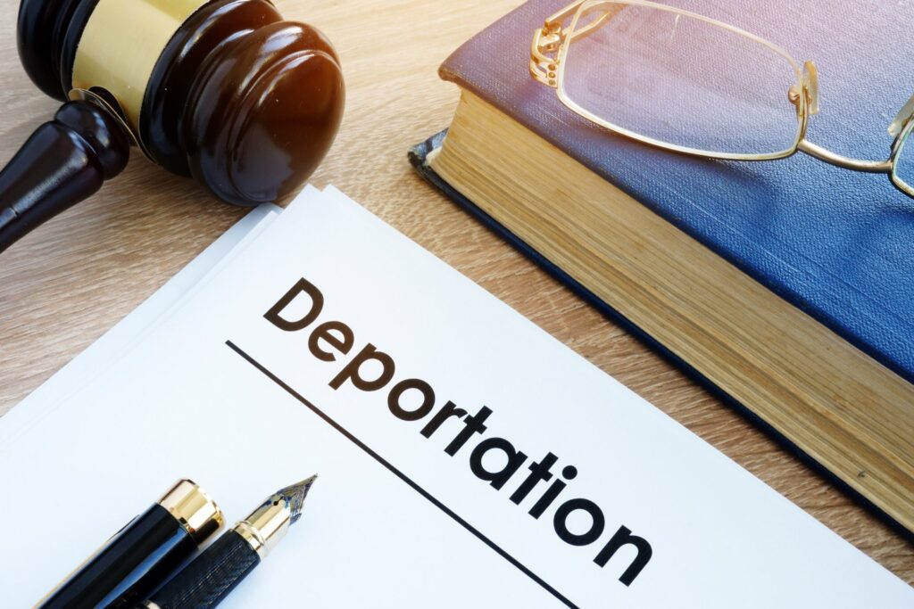 A gavel next to a book with glasses on it next to paperwork and pens that say deportation