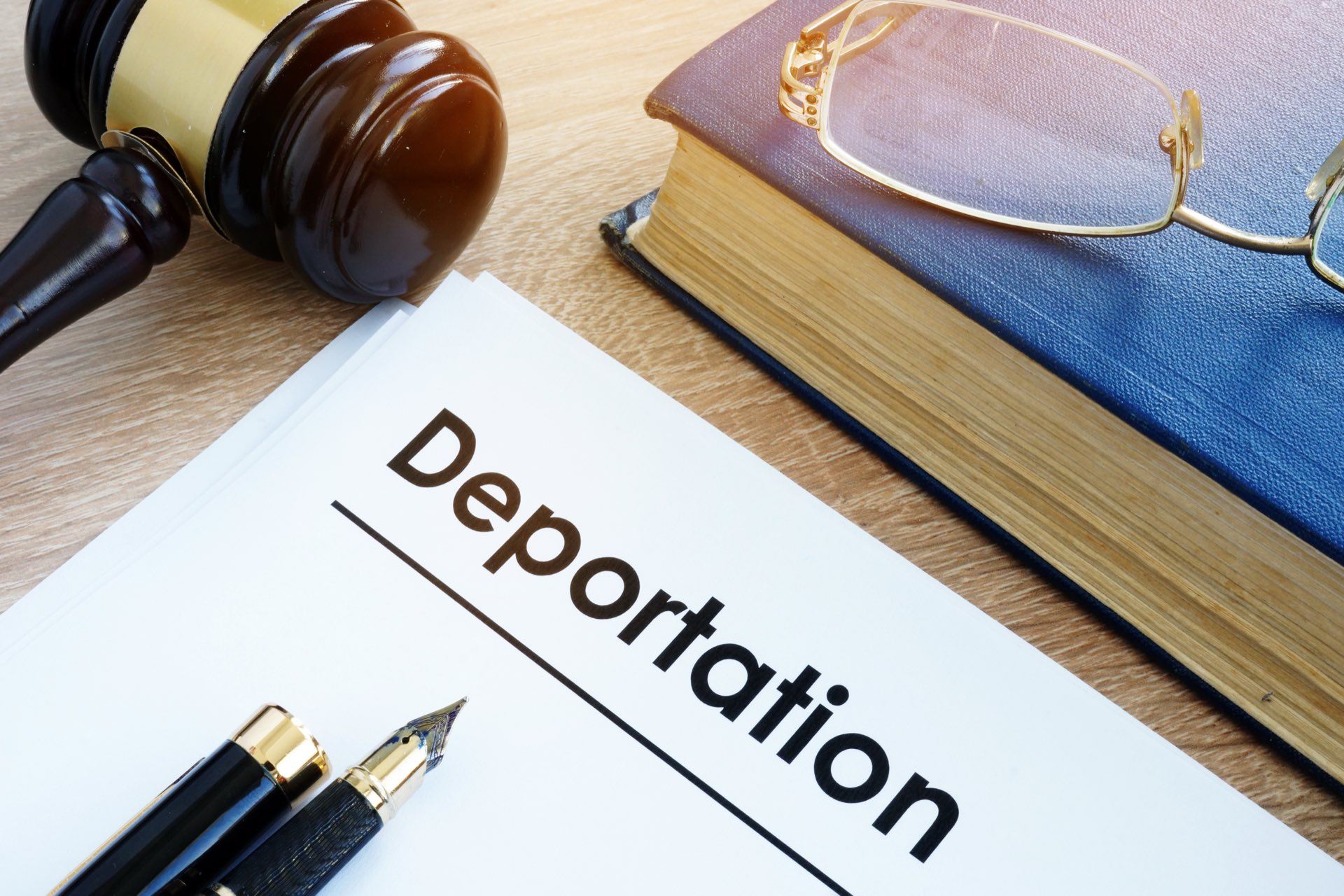 A gavel next to a book with glasses on it next to paperwork and pens that say deportation