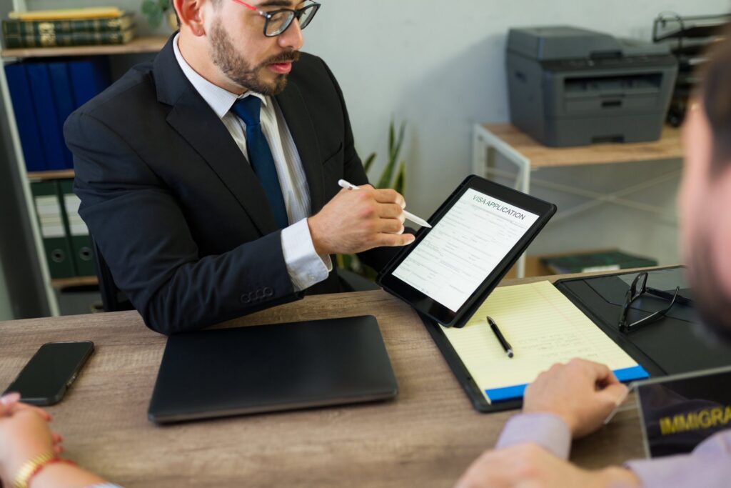 Two people sitting at a desk one is holding an ipad and a pen showing it to the other person