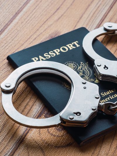 A pair of silver handcuffs laying a blue American passport on a wooden desk