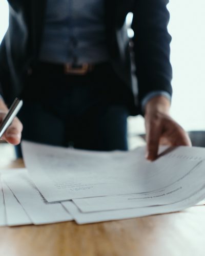 Close up hands signing documents in a modern office with window in background. Pen in hand, papers on the wooden desk, futuristic background.